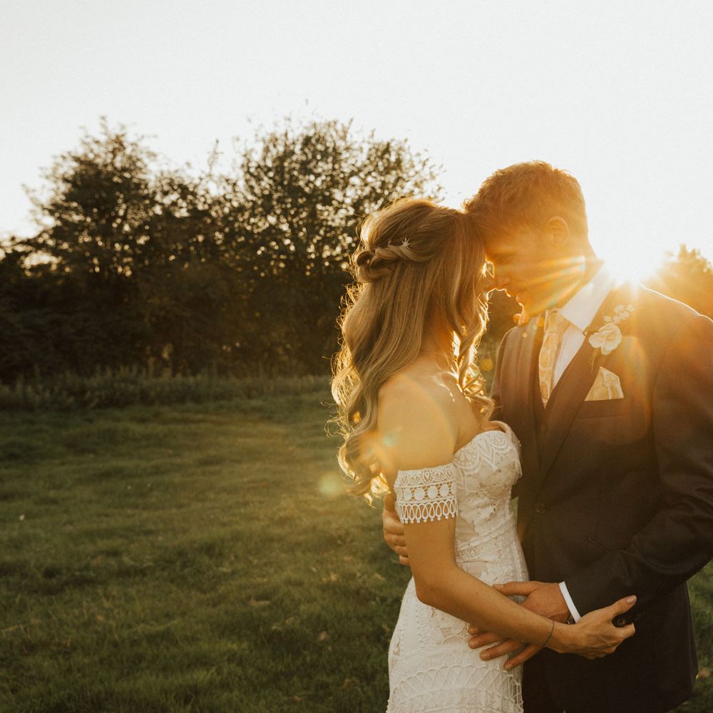 Boho bride and groom in bespoke navy suit embrace during golden hour at Tythe Barn wedding