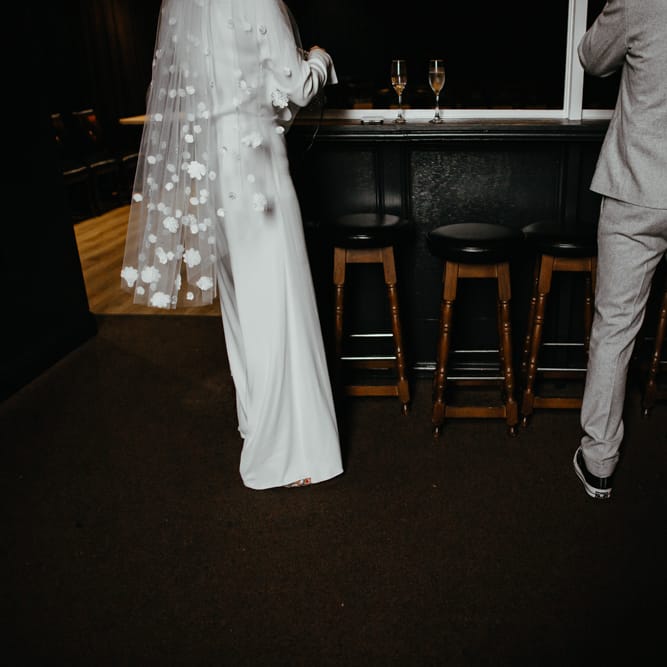 Groom in a grey suit and trainers and bride in a jumpsuit and appliqué veil for DIY wedding 