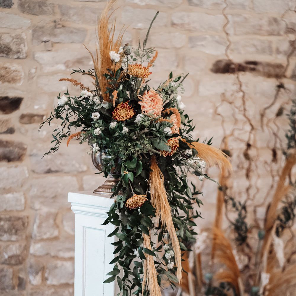 Orange and green foliage floral arrangement on a plinth 