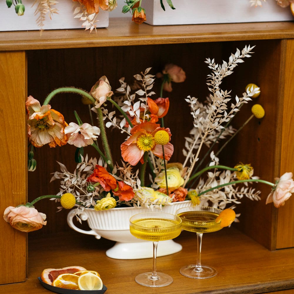 Orange and yellow dried and fresh flowers on mid century modern wedding decor with champagne coupes