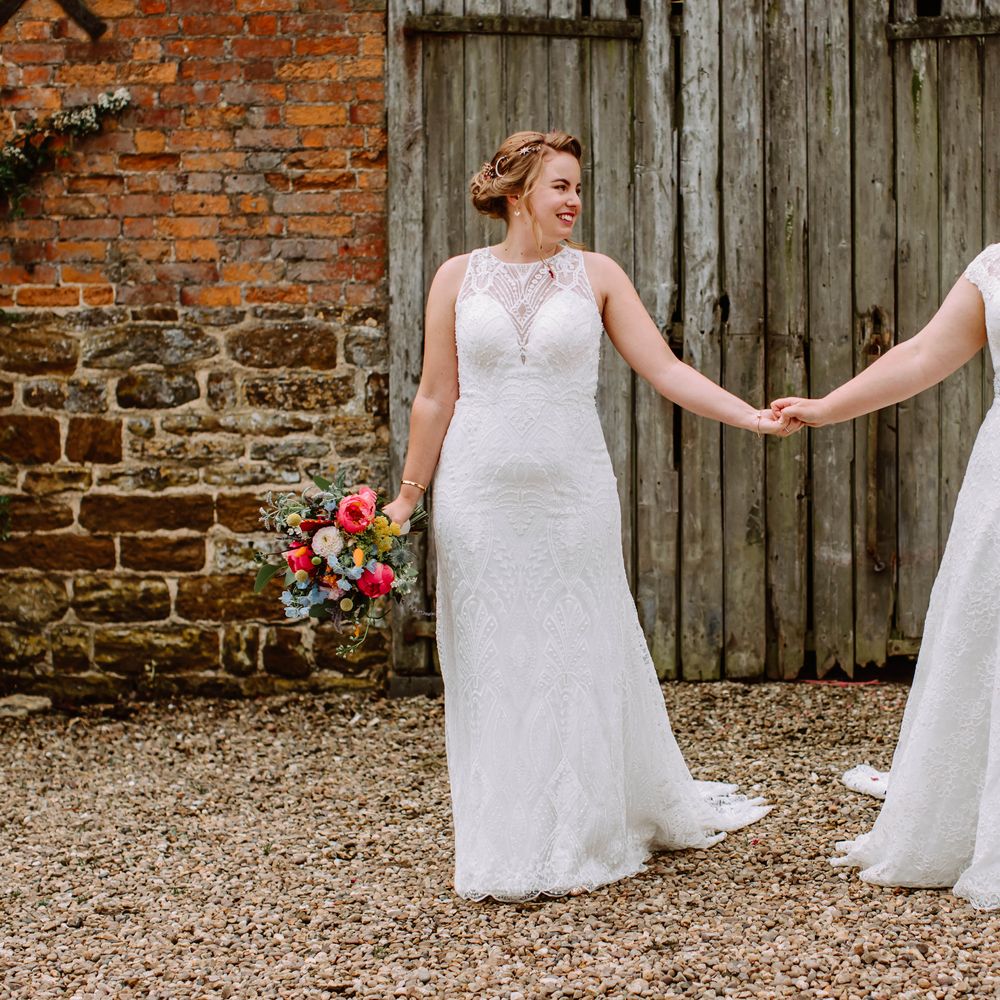 Brides look lovingly at one another as they hold hands and smile on their wedding day 