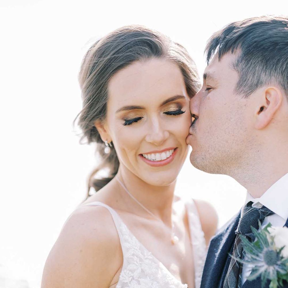 Groom kissing his bride with shimmering gold eyeshadow and false eyelashes wedding makeup 