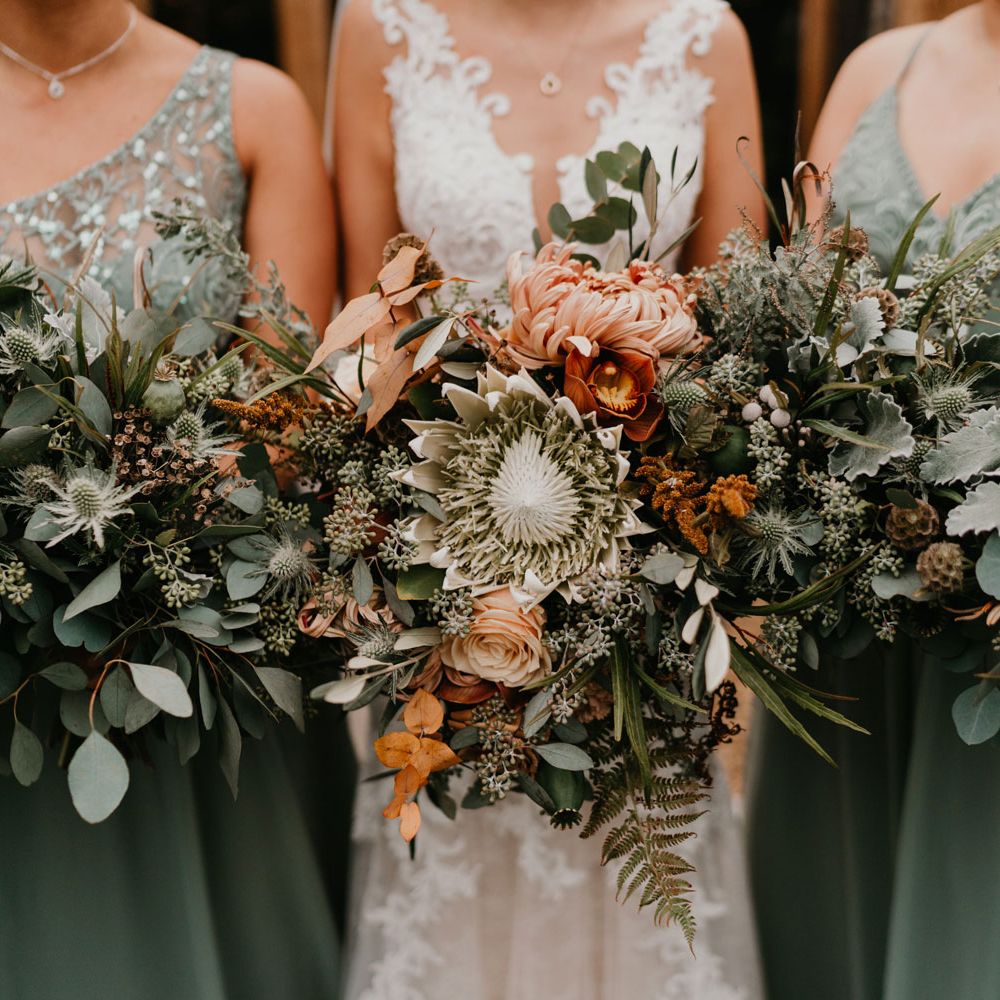 Bride in lace wedding dress and bridesmaids in sage green bridesmaid dresses hold green mixed thistle bouquets
