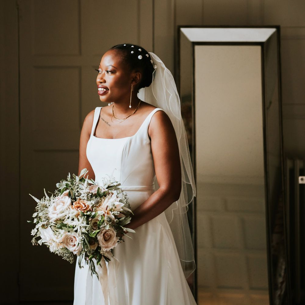 Black bride with short hair decorated with peal clips in an Essense of Australia wedding Dres with straps looking out the window 