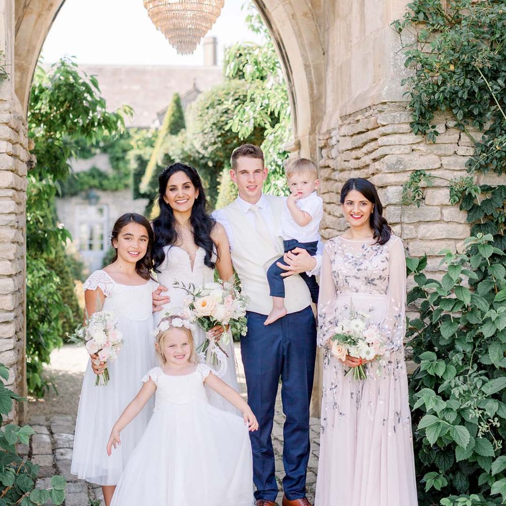 Bride & groom stand with wedding party under archway and chandelier outdoors on their wedding day 