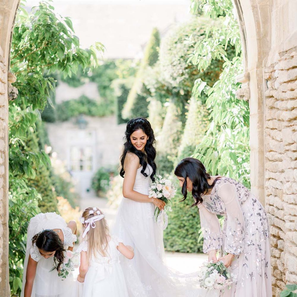Bride stands with her wedding party outdoors as they move her wedding gown train outdoors 