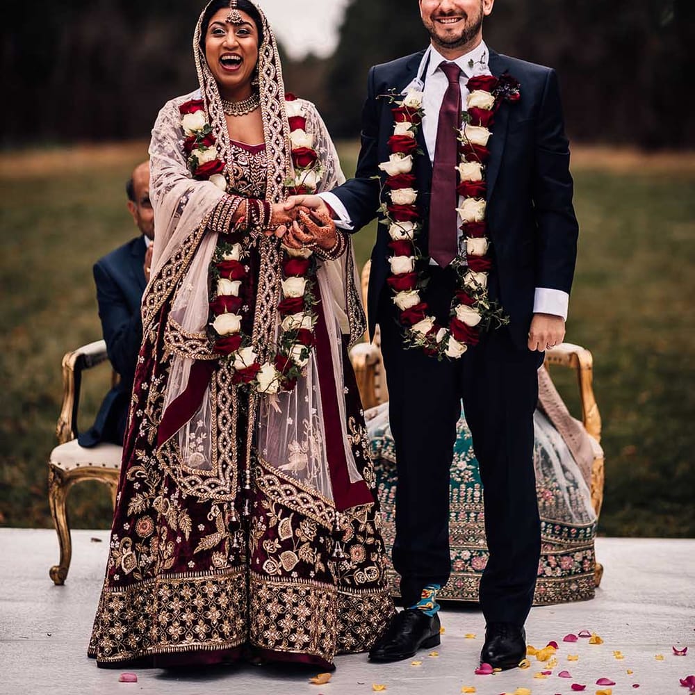 Bride wears Indian burgundy saree wedding dress and groom matches in his burgundy tie adding a pop of colour at his socks