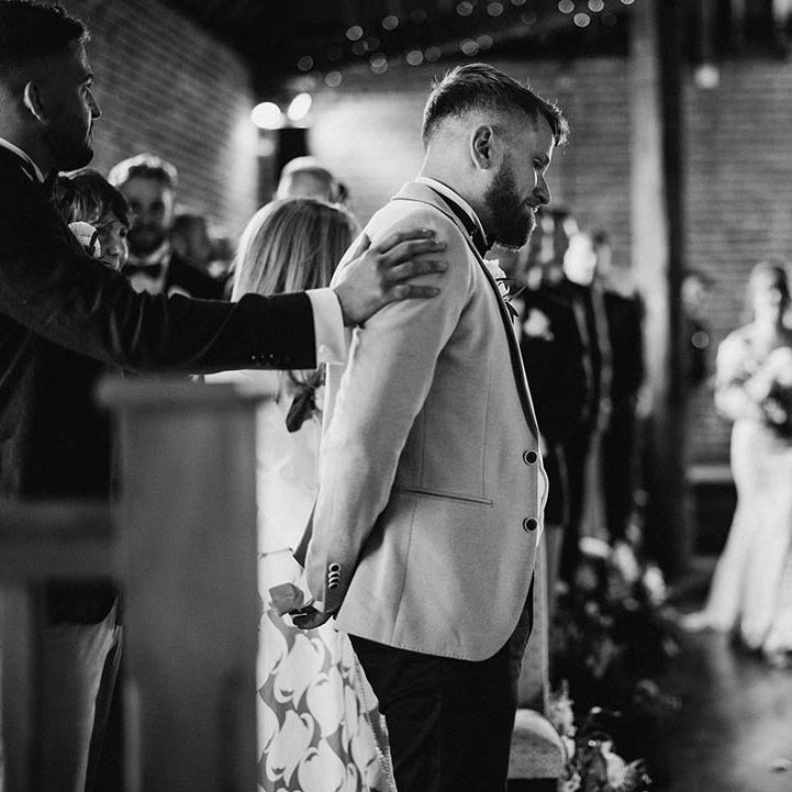 Groom gets ready to see his bride for the first time as she walks into rustic barn wedding