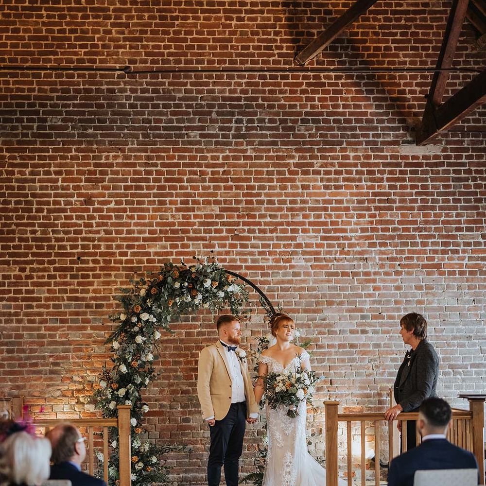Bride and groom at the altar with white and orange coloured wedding flowers at rustic barn 