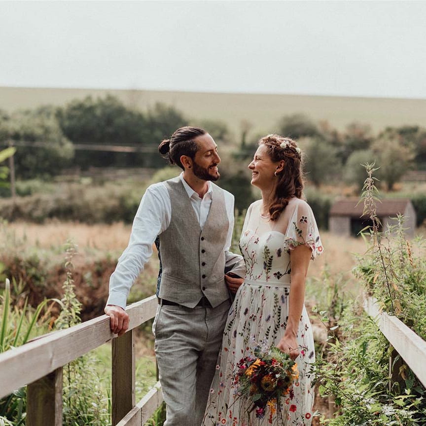 Bride and groom smiling together with bride holding colourful pink, purple, red, yellow, orange wedding bouquet 