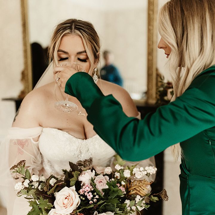 Bride has a quick drink of courage before the ceremony as bridesmaid in emerald green dress lifts the glass