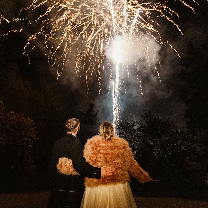 Bride and groom stand with their arms around each other as they watch the firework entertainment