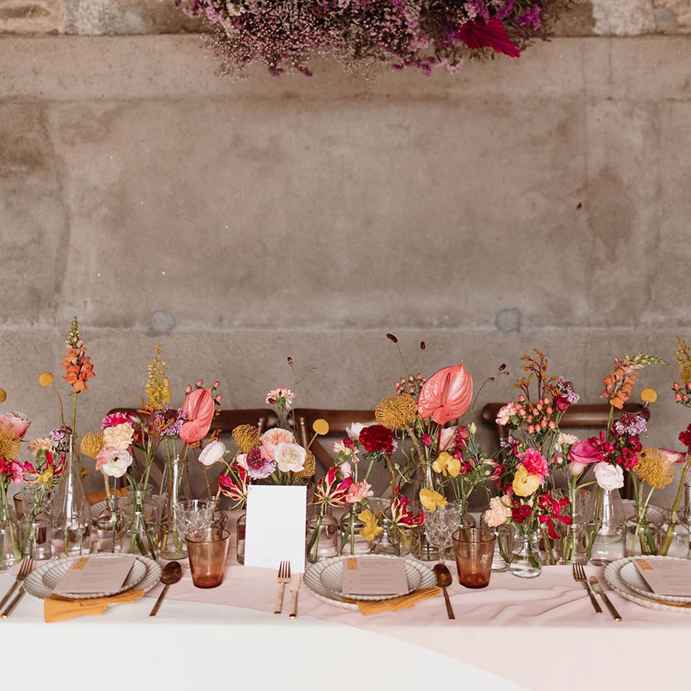Anthurium, carnation and rose flower stems in bottles to decorate the wooden table with a flower cloud installation handing above 