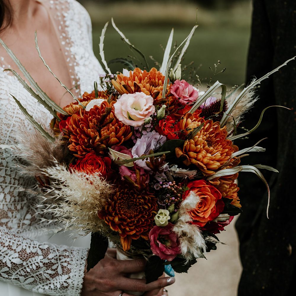 Orange, red, pink and purple wedding flowers with dried grass bouquet for autumnal wedding at Silchester Farm 