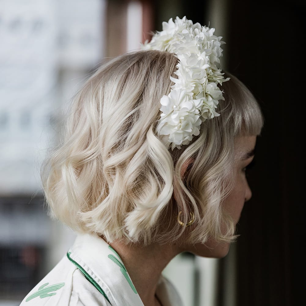 Bride wears white flower headband with pearls on her wedding day as she gets ready in cactus print robe