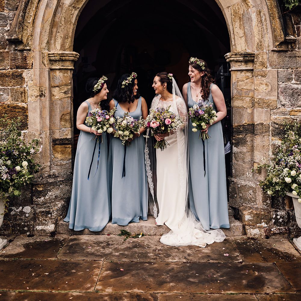 Bride laughs with her three bridesmaids in blue dresses and matching flower crowns 