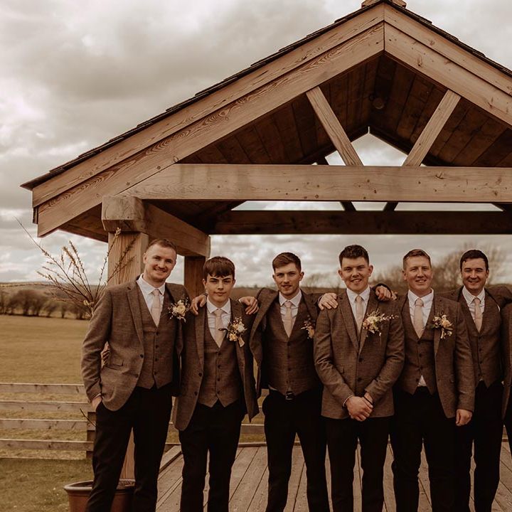 Groom with groomsmen in matching three piece brown suits posing outside at Eden Barn