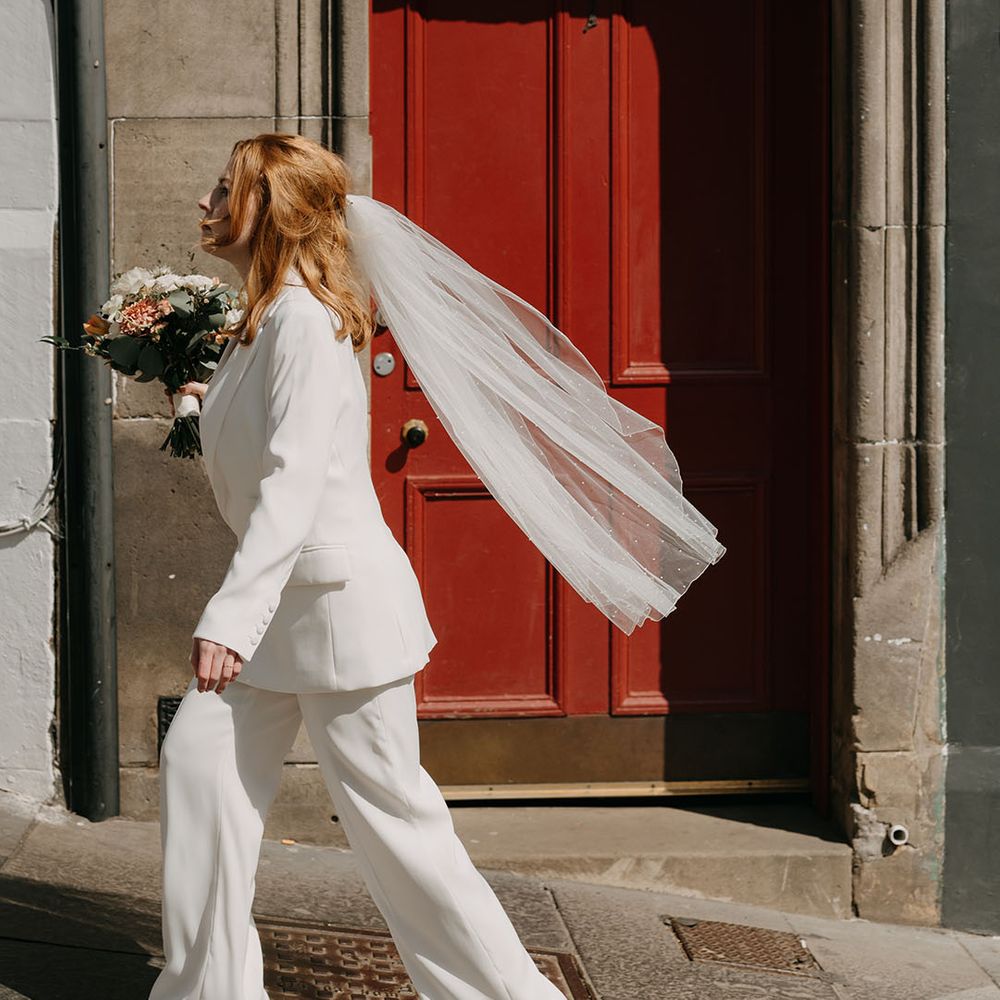 Brides veil blows behind her on her wedding day as she wears bridal suit