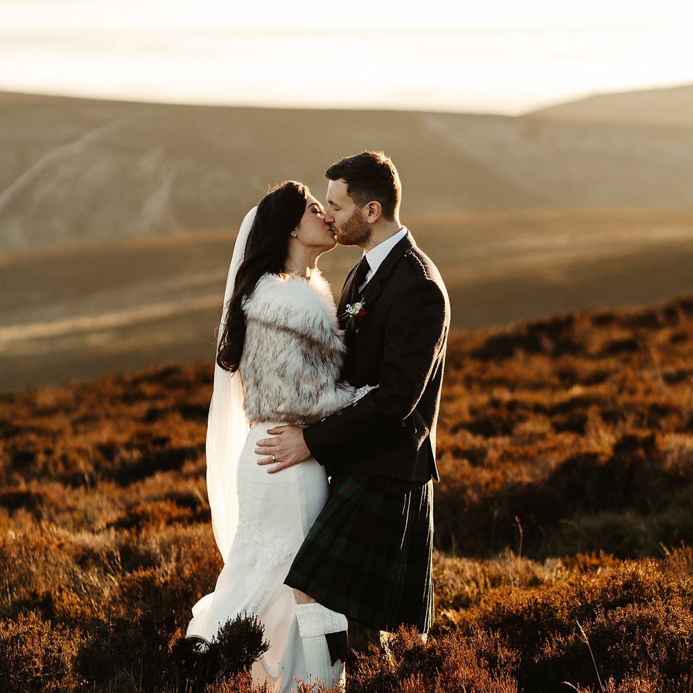 Bride & groom embrace on Scottish hills during sunset on their wedding day