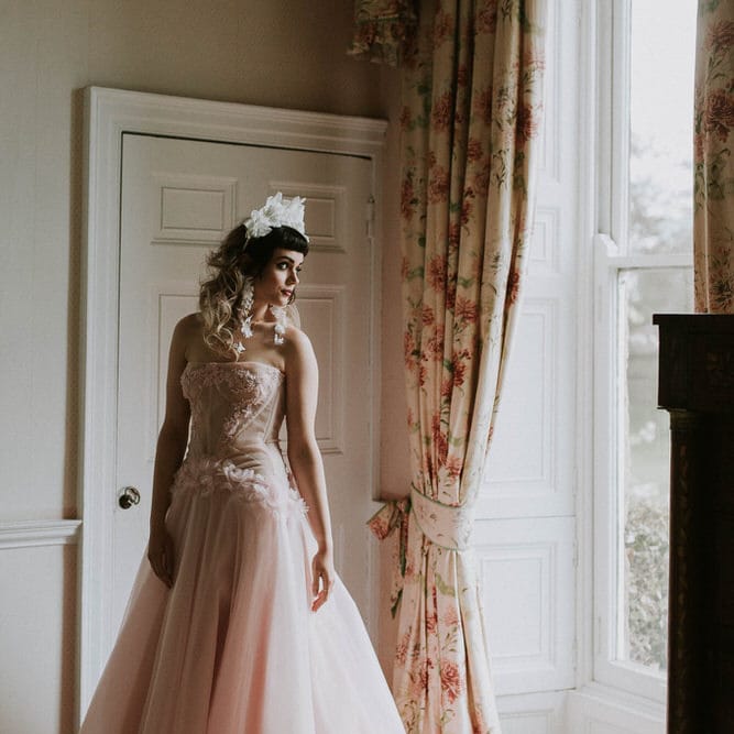 Bride in a 3D flower headband and a pink strapless wedding dress with corset bodice, appliqué detail and tulle skirt 