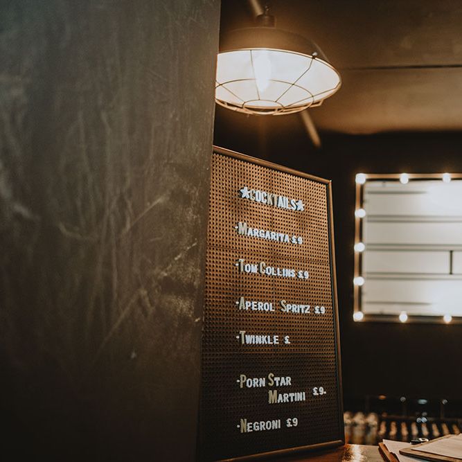 Cocktail menu at Scale Liverpool complete with vintage signage in the background surrounded by lights