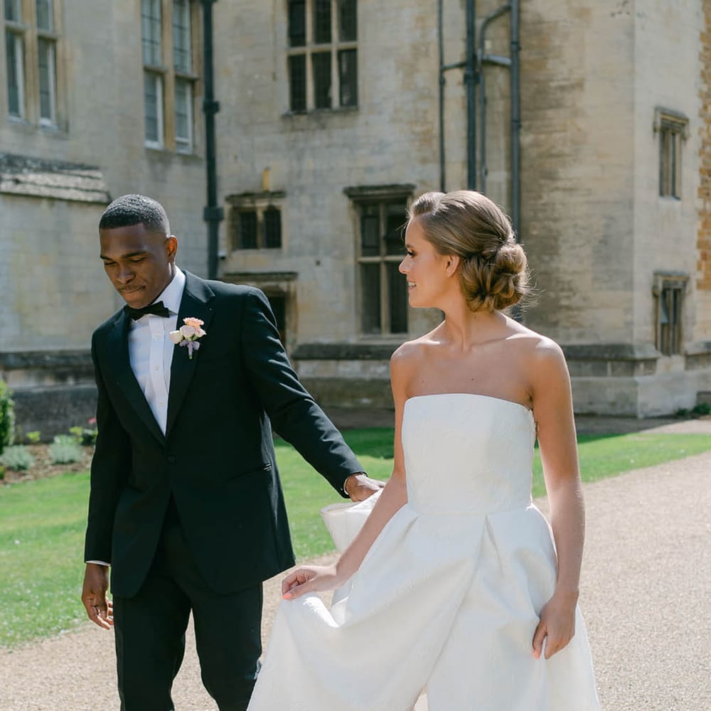 Bride in strapless Jesus Peiro wedding dress walking with the groom in black tie around the grounds of Rushton Hall 