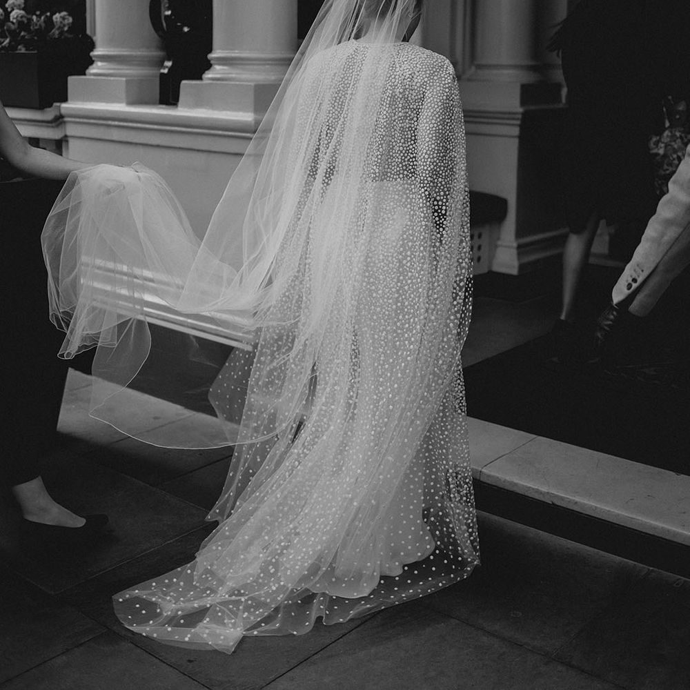 Bride in sparkly dotted Jesus Piero wedding dress and cape walking into her wedding 