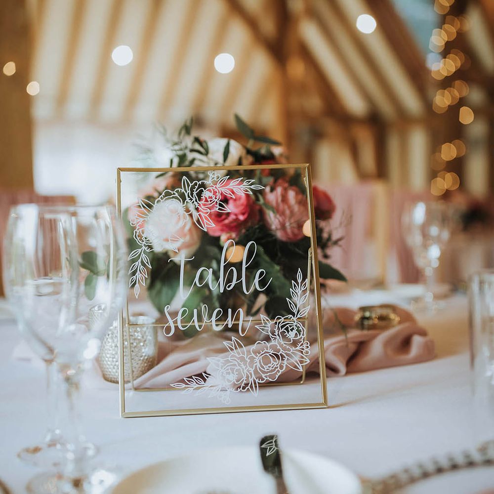 Gold photo frame table name on a white tablecloth with pink flower centrepiece