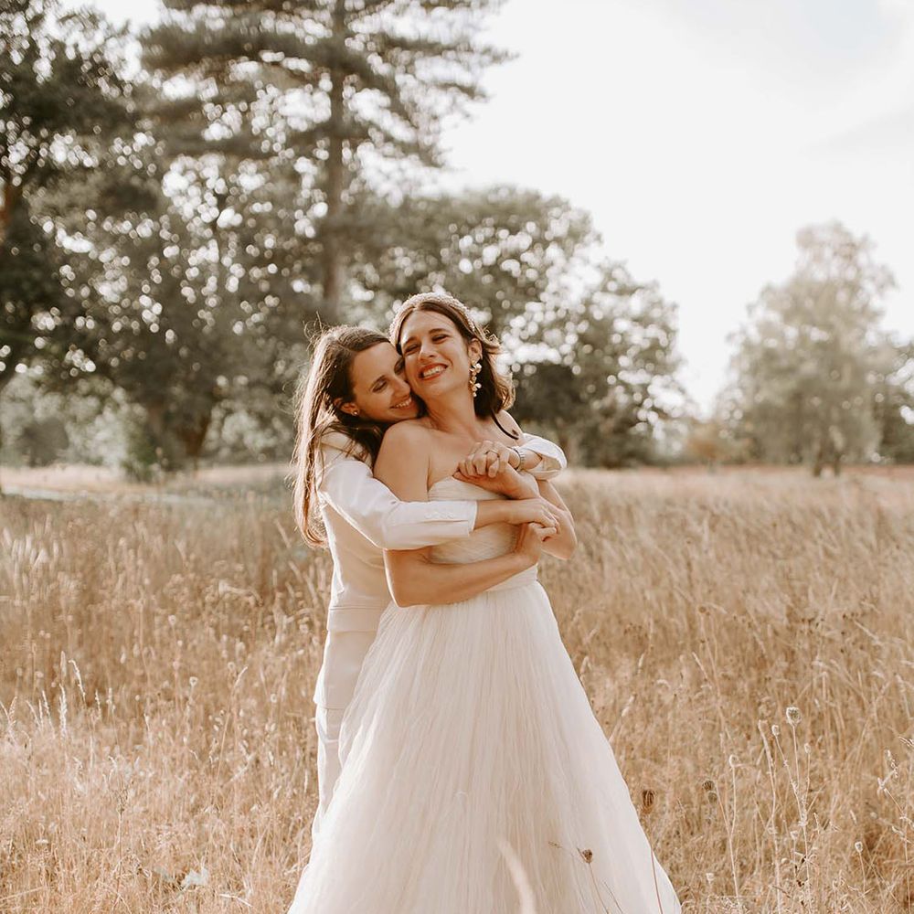 The brides share an intimate embrace in a field for their wedding at the Wilderness Reserve 