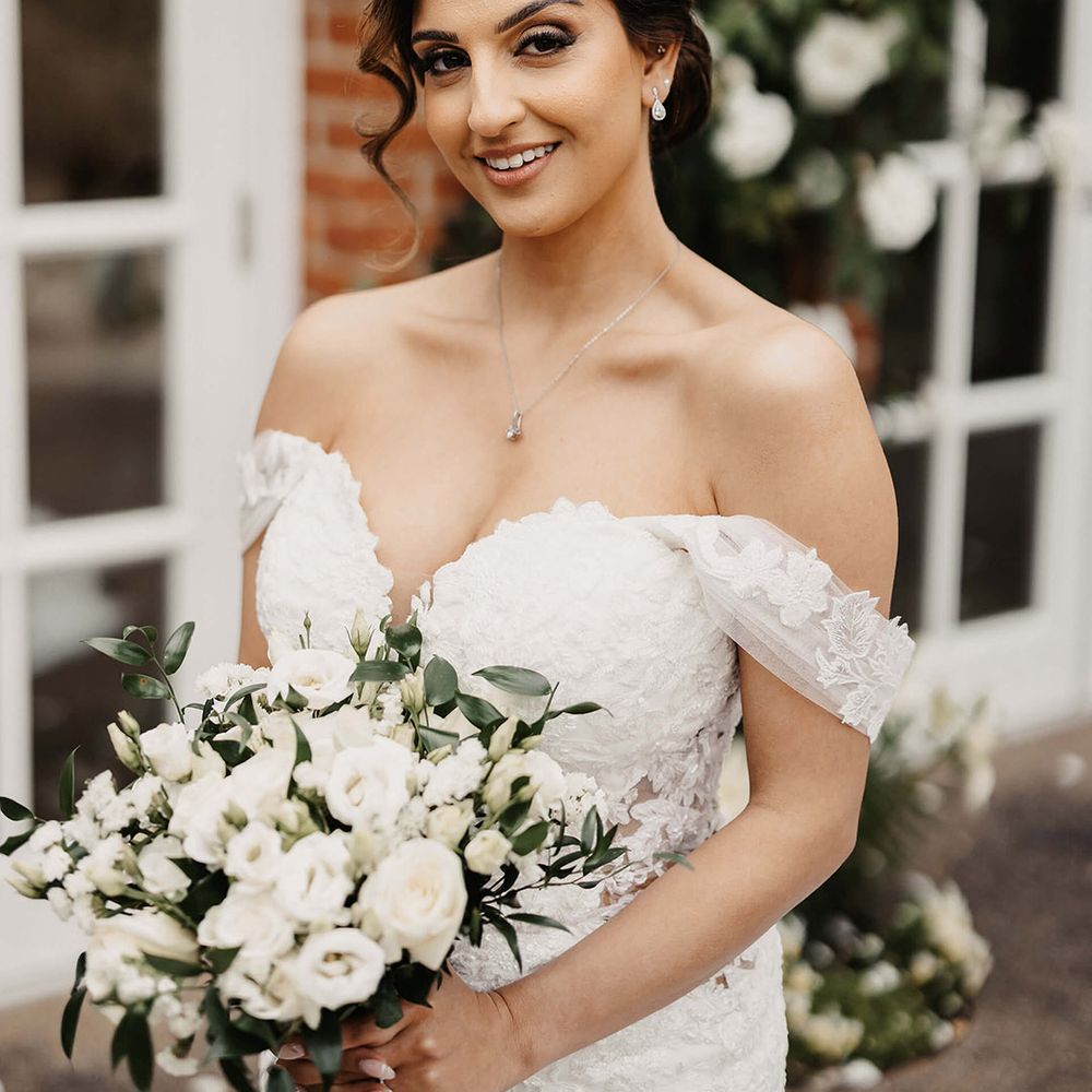 Bride in a flower lace wedding dress with a white bouquet and hair in an updo complete with silver jewellery