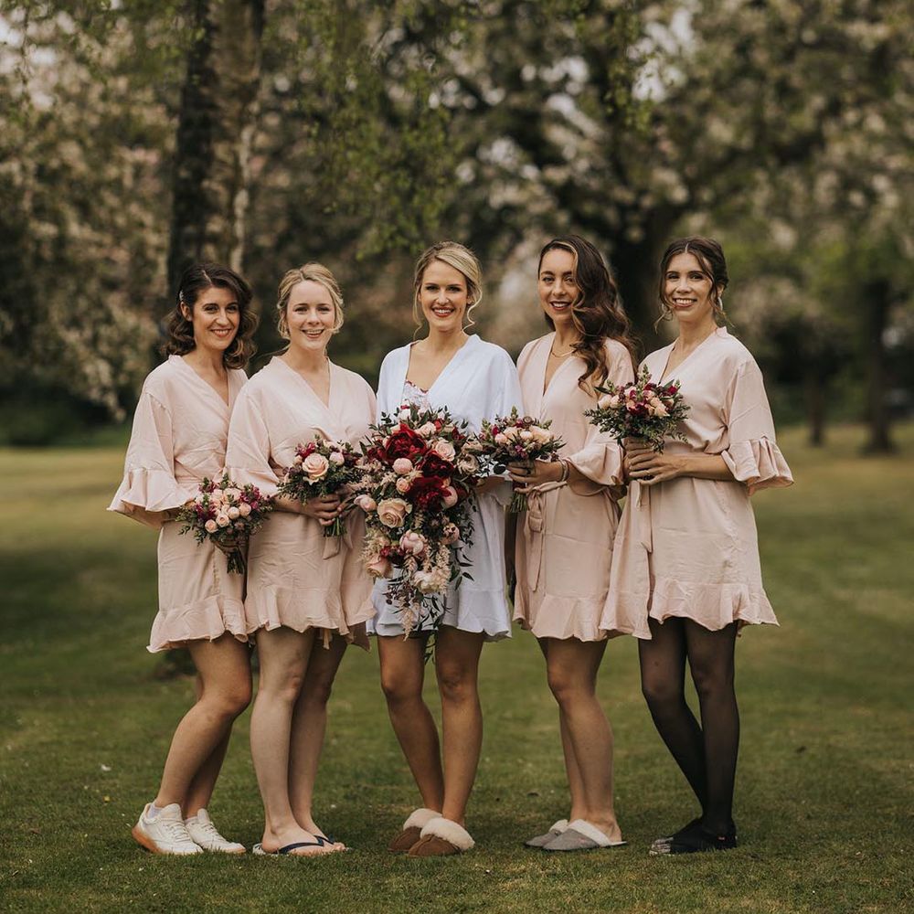 Bridesmaids in ruffle pink robes holding their small bouquets with the bride in a white robe holding a large cascading bouquet