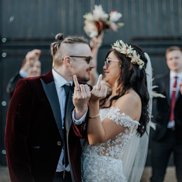 The bride in sunglasses and a flower crown shows off her ring finger with her new wedding ring on with the groom for fun couple portrait 