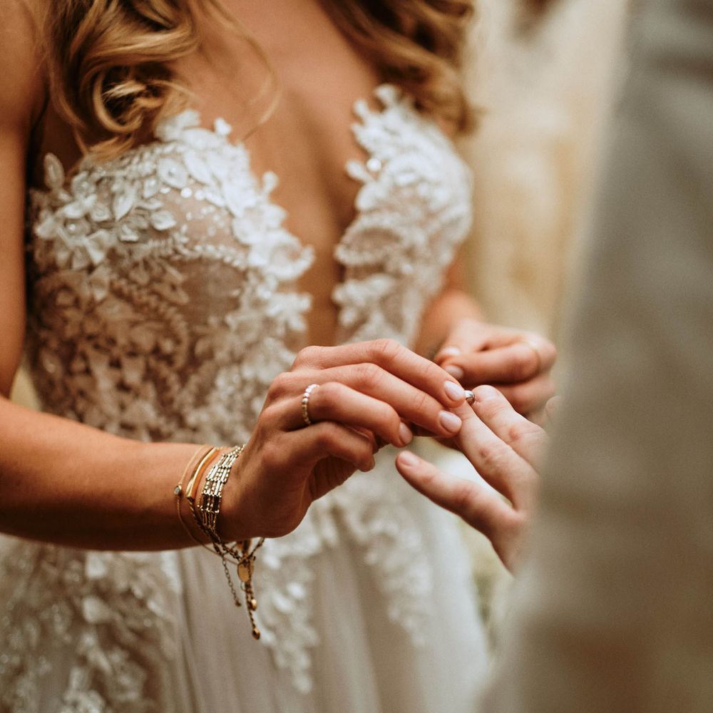 Bride in white embroidered low cut wedding dress exchanging rings with groom