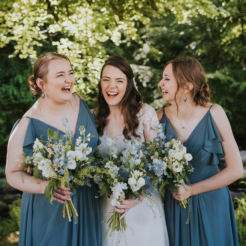 Bridesmaids in matching blue ruffle bridesmaid dresses with the bride in beaded wedding dress holding white and blue bouquets 