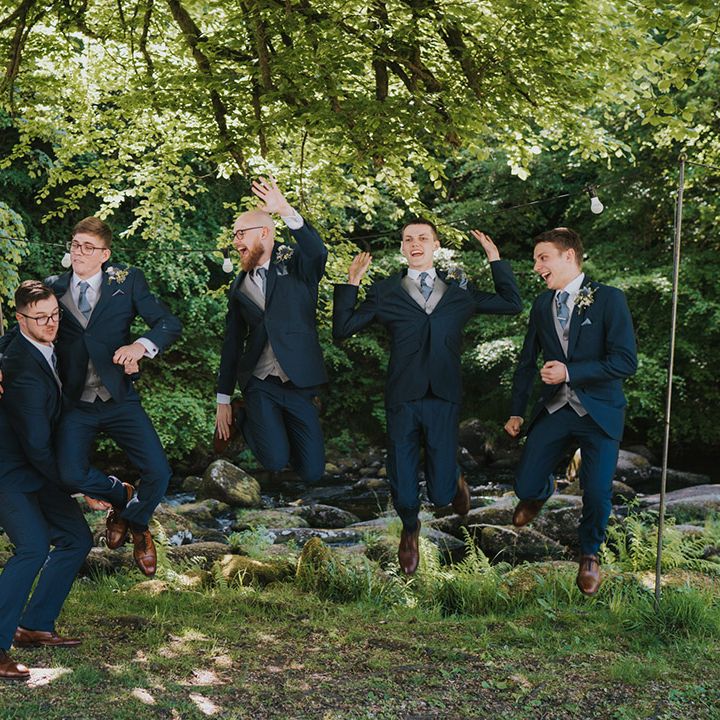 Groomsmen all jump in the air for fun wedding photo in navy wedding suits for blue theme wedding