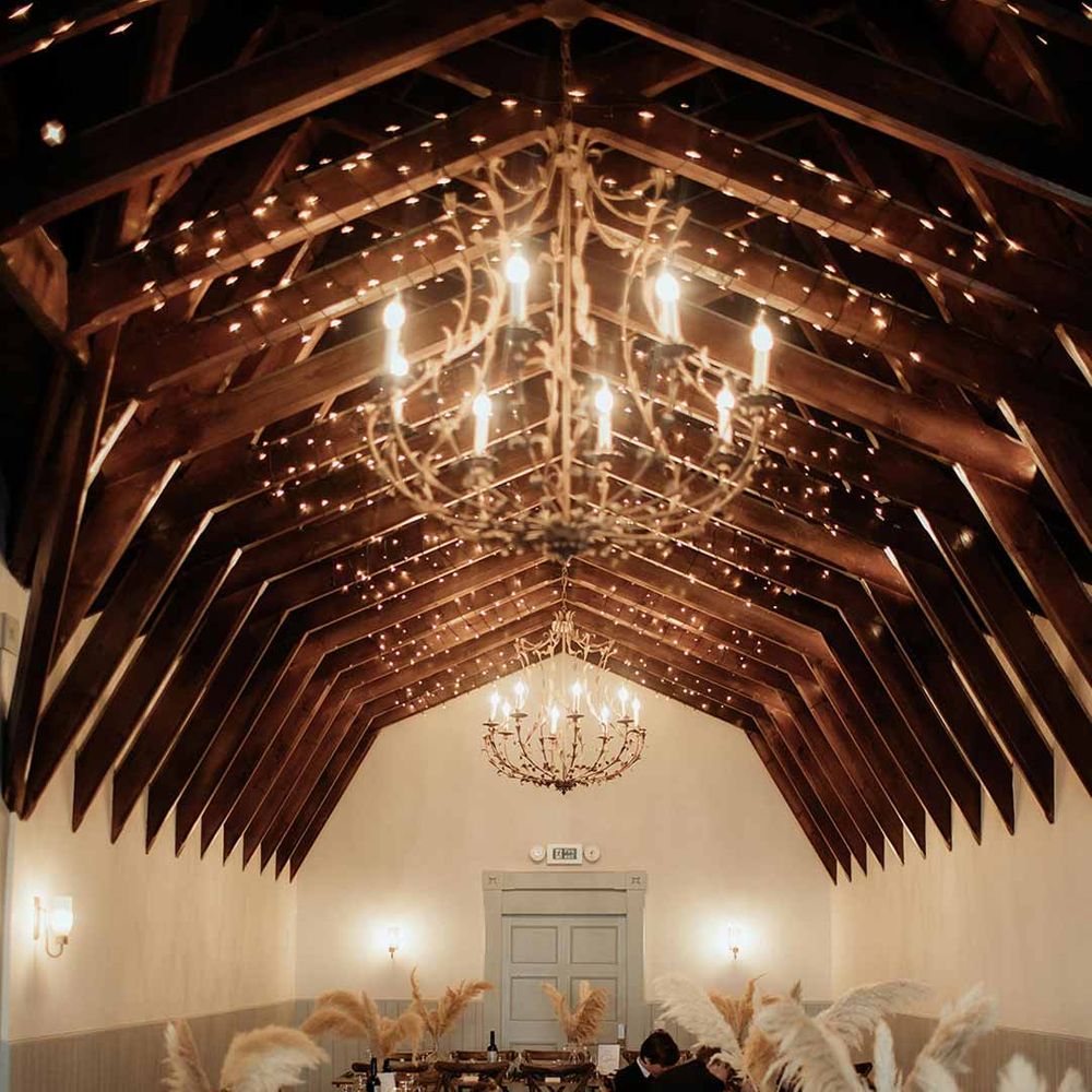 Reception room of The Dougarie Boathouse wedding venues Scotland with fairy lights, large chandeliers and pampas grass table centrepieces 