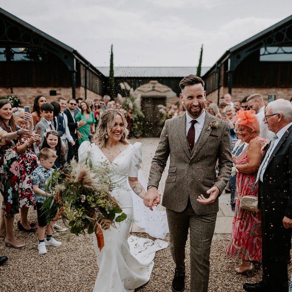 Bride in puff sleeve wedding dress walking out to confetti with the groom 