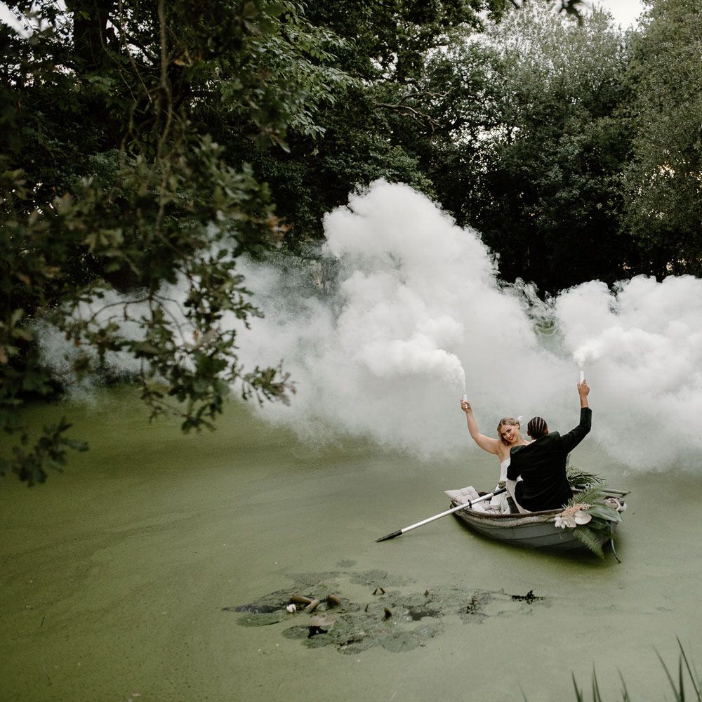 Bride and groom letting off white smoke bombs on a green lake for tropical wedding theme