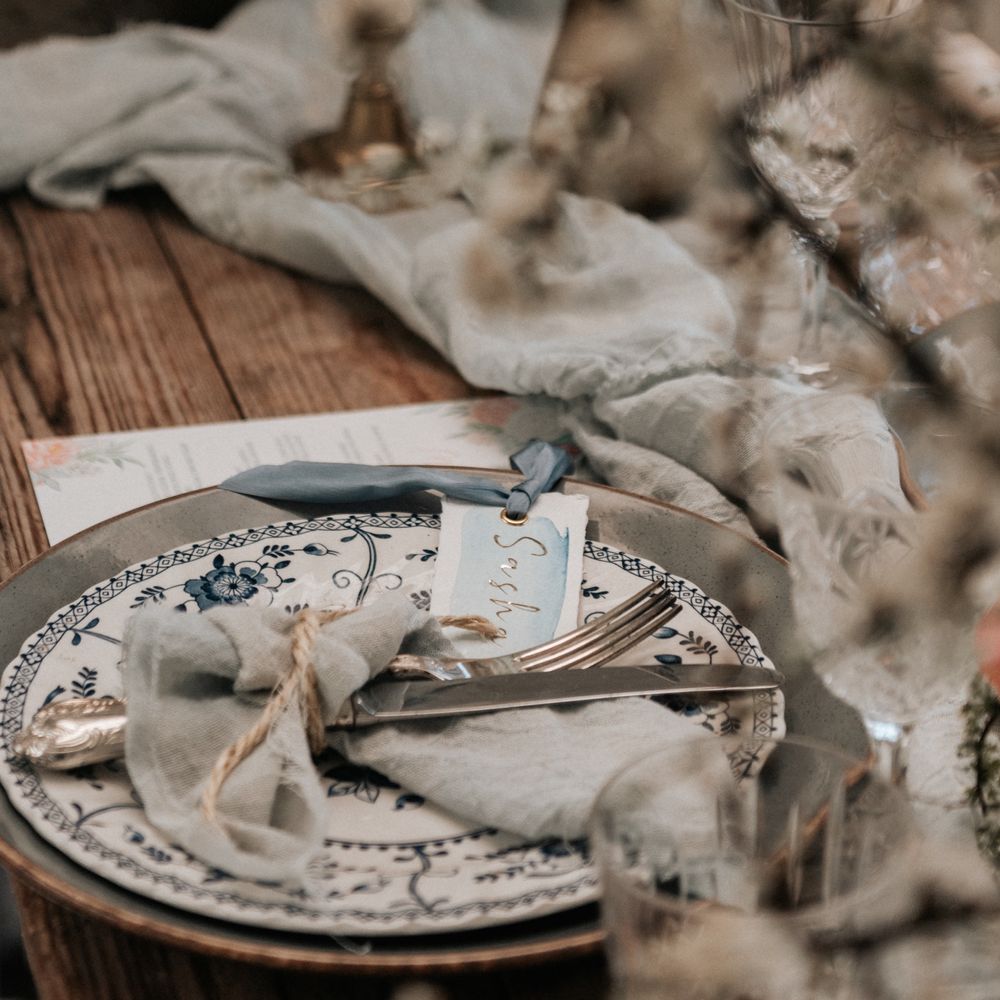 Pale grey plates with floral pattern, and pale blue napkins tied with brown string