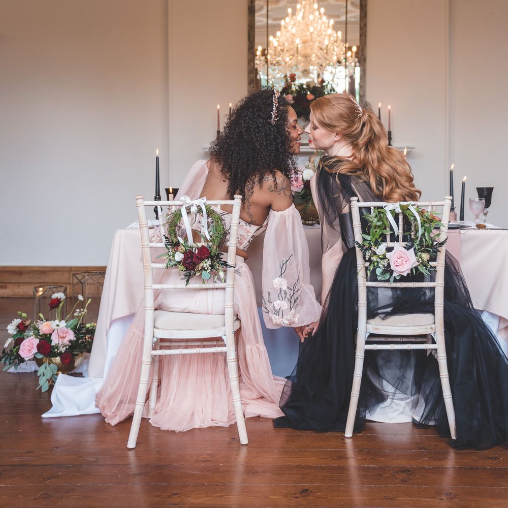Two brides in coloured wedding dresses kissing at their intimate wedding reception at Thicket Priory