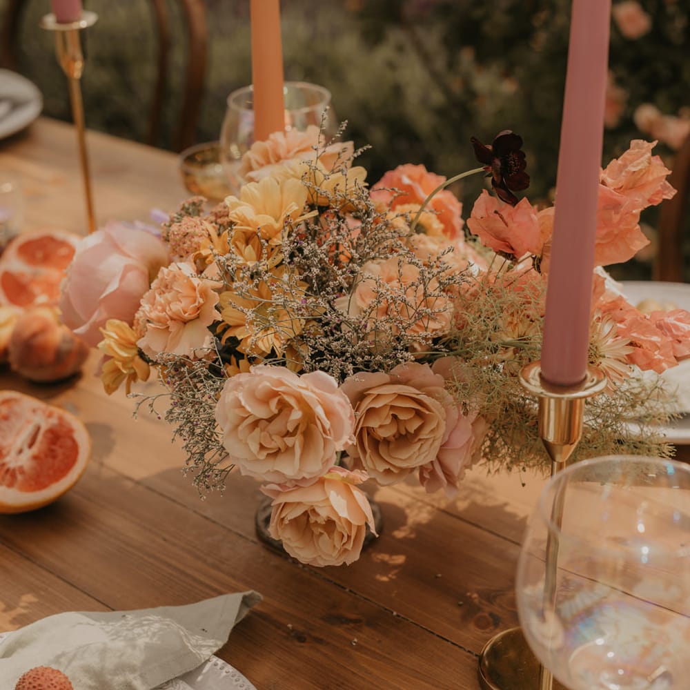 Pastel orange, peach, coral and yellow wedding flower arrangement at outdoor wedding reception 