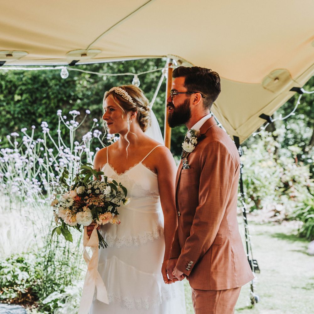 Bride & groom smile as they marry under tipi on a bright & sunny day in Cornwall 
