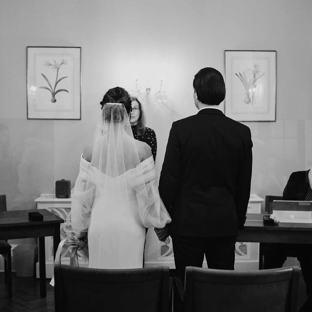 Brides chiffon veil flows as she stands hand in hand with groom in Chelsea Town Hall 