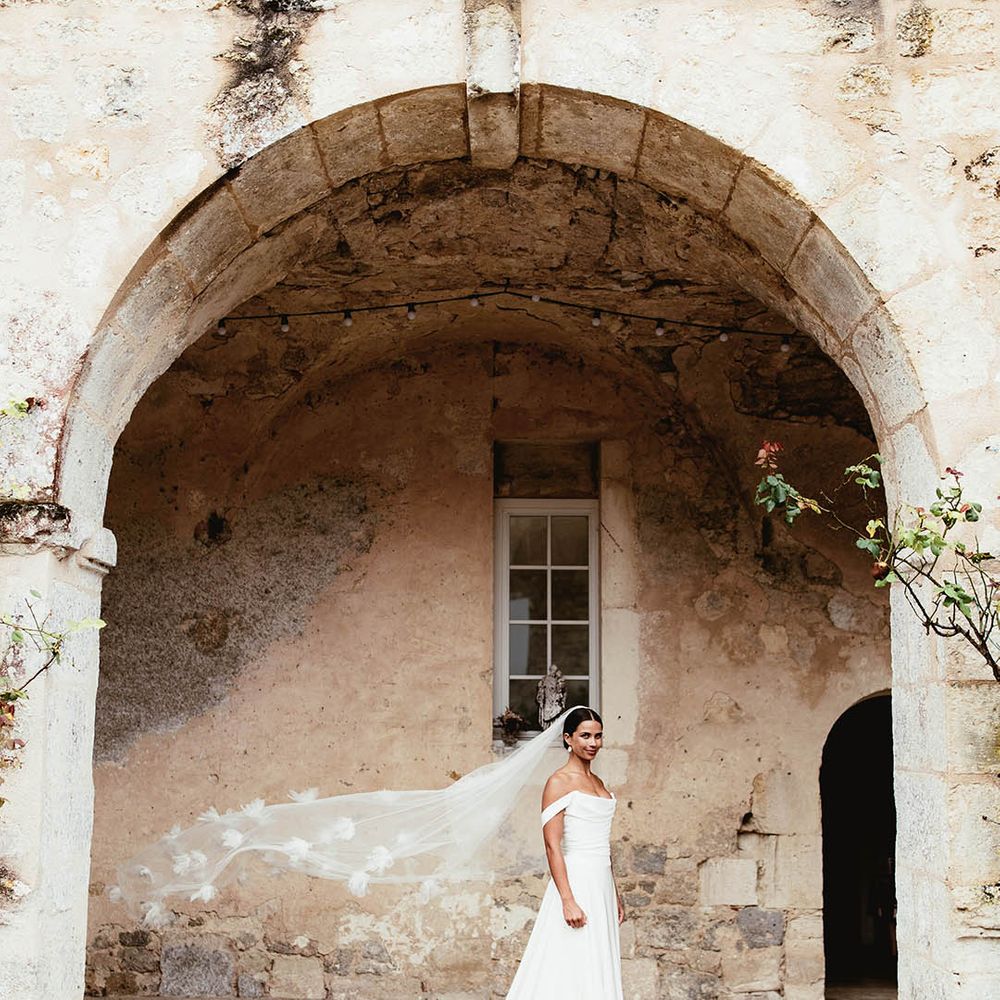 Brides veil blows in the wind as she stands under archway outdoors 