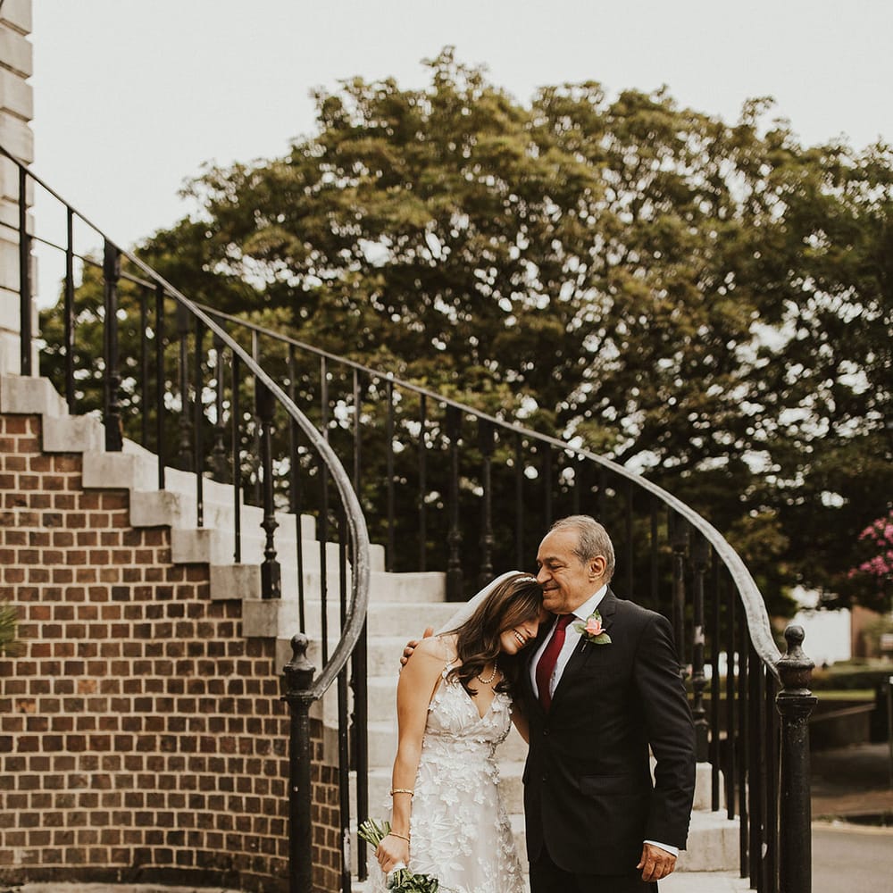 Bride leans her head into fathers shoulder on her wedding day as he wraps his arm around her