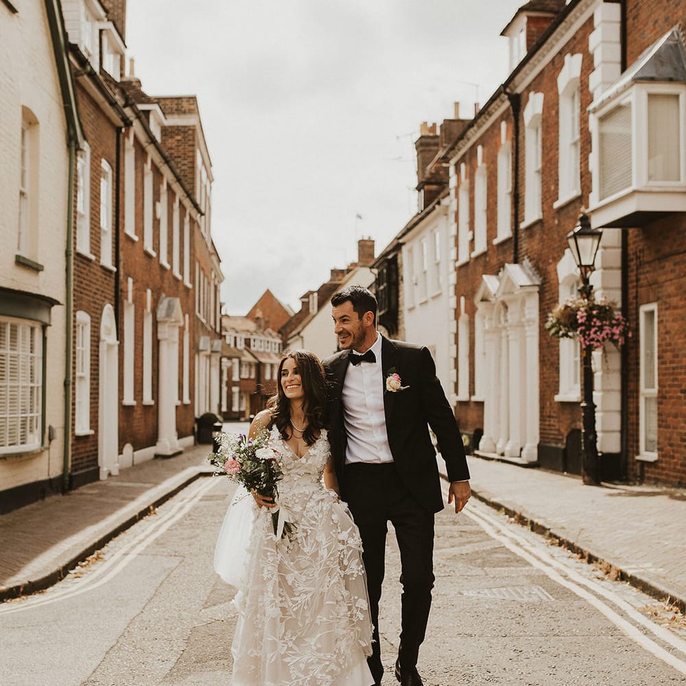 Bride & groom walk through streets as bride carries pink bouquet