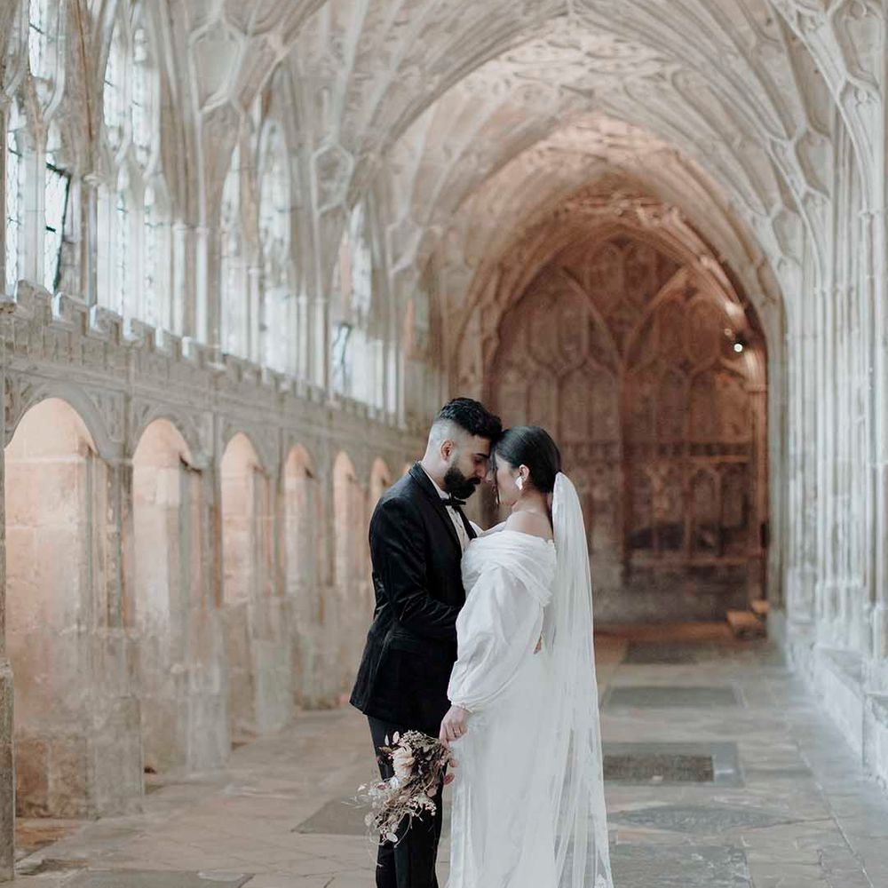 Portrait of the groom in a tuxedo and his bride in an off the shoulder wedding dress and lace embroidered cathedral length veil at the Blackfriars Priory 