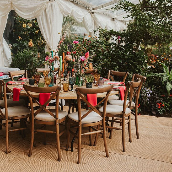 back garden wedding in a clear marquee with round wooden tables decorated with colourful linen, candles and flowers 