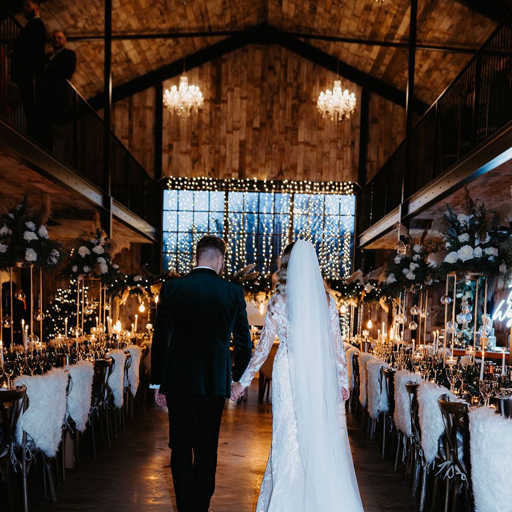 Bride and groom enter fairy lights wedding reception with fur details, white candles and other festive touches for Christmas wedding 