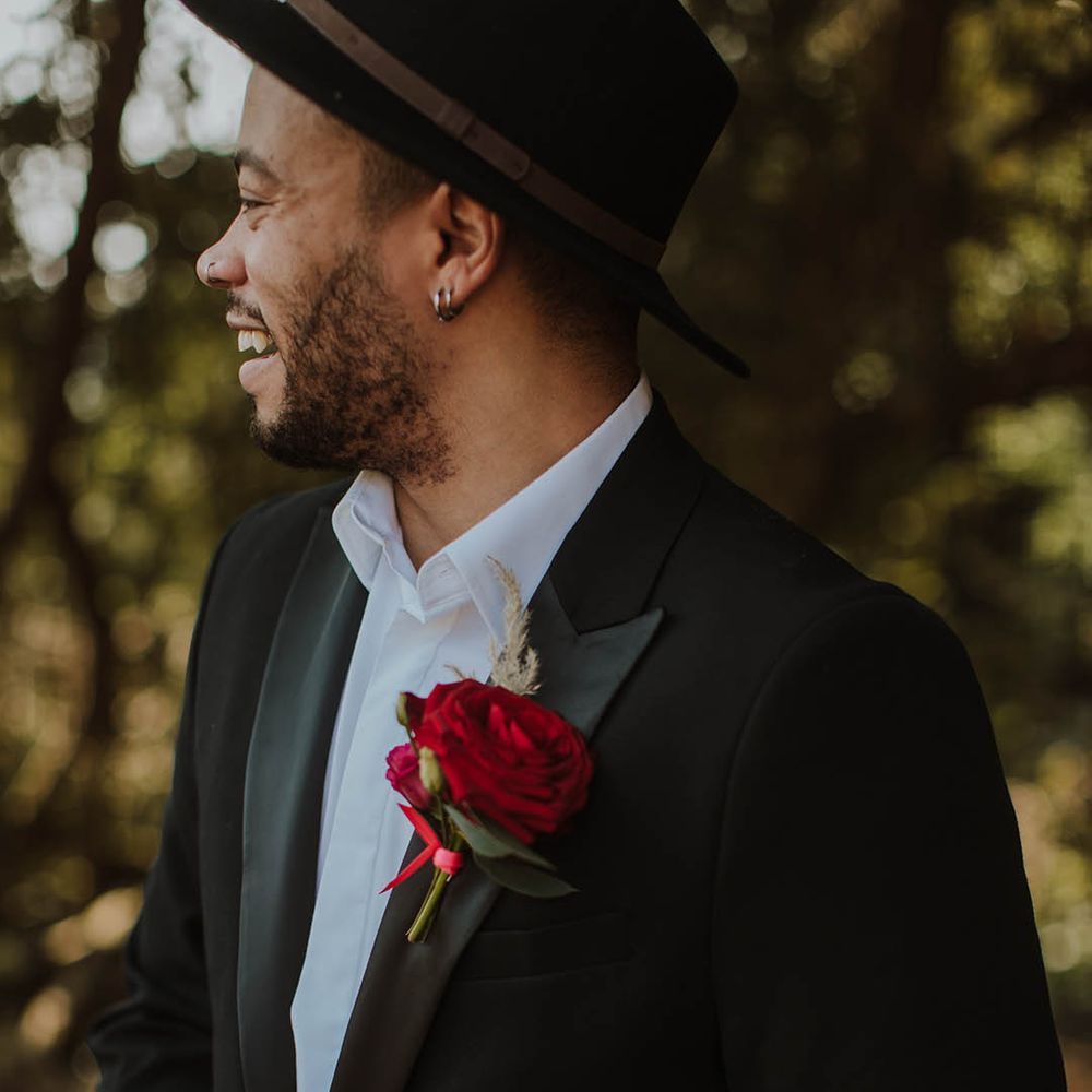 Groom in a black suit jacket with satin lapel, red buttonhole flower and open collar white shirt at Prestwold Hall wedding 